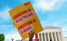 Hand holding sign in the air that reads: Abortion is healthcare. Abortion is a right. 