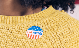 Cropped photograph of a person wearing a yellow sweater with a ¡Ya voté! sticker