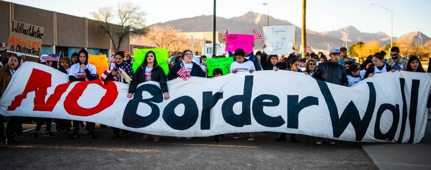 protesters holding a sign that says "no border wall"