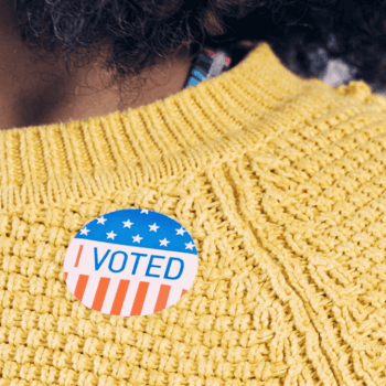 Picture of person in yellow sweater wearing an I voted sticker