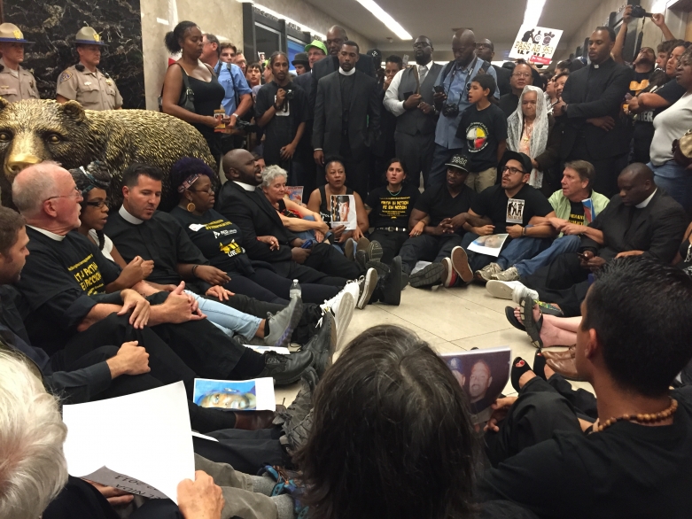 Protestors sit and stand in a circle outside Governor Brown's office