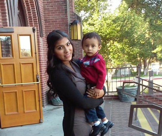 Angelica stands on the steps in front of her school, holding her son Joel