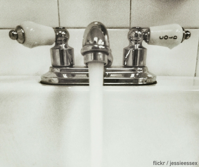 Black and white image of water flowing out of a tap into a porcelain sink