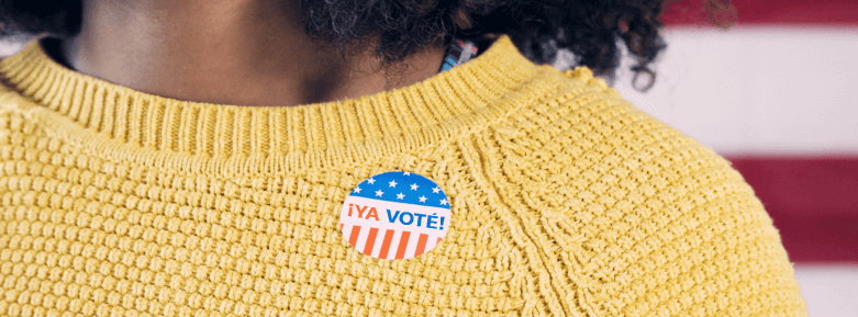 Cropped photograph of a person wearing a yellow sweater with a '¡Ya voté!' sticker