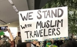 Sign in a crowd protesting the ban at SFO airport reads, "We stand with Muslim travelers"